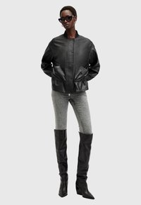 Zwart leren bomberjack met ribbeldetails, gecombineerd met grijze skinny jeans en zwarte laarzen tot de knie, met een punttip en blokhak.