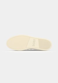 Semelle d'une chaussure décontractée beige avec une adhérence texturée et le mot « BOSS » embossé au centre sur un fond uni.