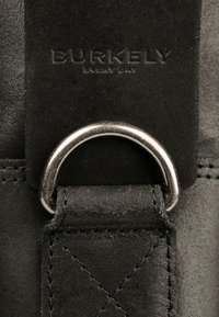 Schwarzer Ledergriff mit geprägtem "BURKELY EVERY DAY"-Logo, ausgestattet mit einem silbernen Metallring und einem Rautenmuster auf einer Seite.