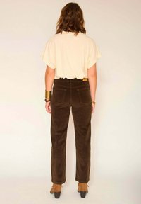 T-shirt beige oversize rentré dans un pantalon en velours côtelé marron foncé taille haute avec des jambes droites. Des bottes à talons marron visibles.