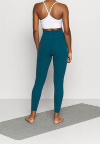 Tealfärgade, högmidjade leggings och en vit sportbh, båda åtsittande och gjorda av elastiskt material, visade på en yogamatta.