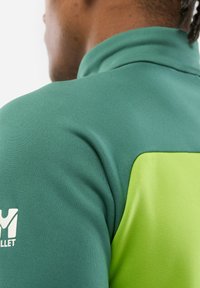 Green and light green pullover with a high collar, made of textured fabric. Features a logo in white on the left sleeve.