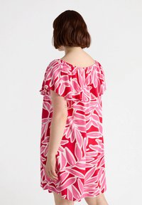 Kurzes pinkes Kleid mit einem gerafften Ausschnitt und kühnen weißen Blattmustern, in lässiger Passform und aus weichem Stoff.