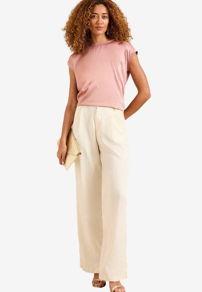 Top rosa chiaro a maniche corte abbinato a pantaloni larghi di colore crema. Tieni in mano una pochette beige. Tessuto morbido con un design rilassato.