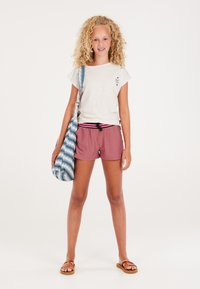 Lichtgrijze korte mouwen shirt met een klein ontwerp, gecombineerd met roze shorts met een zwart en roze trekkoord. Tas met jeanspatroon en sandalen.