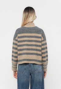 Stripete strikkegenser med grå og beige farger, høy krage, droppede skuldre og cropped design. Teksturert ullmateriale.