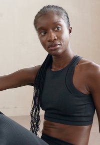 Top deportivo corto negro con un diseño texturizado. La tela suave, el corte sin mangas y el escote alto mejoran la comodidad y la facilidad de movimiento.