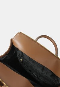 Borsa a tracolla in pelle marrone con chiusura a zip, dotata di un interno a motivi neri e un solo manico superiore. Hardware in tono oro visibile.