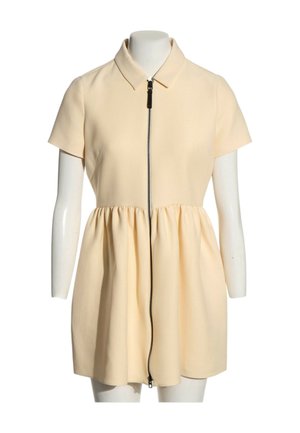 Crèmekleurige jurk met korte mouwen, kraag en geplooide taille, met een zwarte ritssluiting over de hele voorkant.