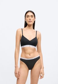 Fekete bralette és hozzáillő, vékony pántos alsó szett. A bralette V-nyakú és rugalmas derékpánttal rendelkezik, melyen a "TOMMY HILFIGER" felirat olvasható.