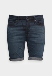 Pantalones cortos de mezclilla azul oscuro con dobladillos enrollados, cinco bolsillos y cremallera. El material tiene una textura suave y un ligero desgastado. Cierre de botón metálico.