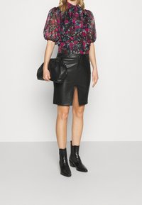Blusa floreale a maniche a sbuffo in tonalità scure, abbinata a una gonna a tubino in pelle nera con spacco davanti. Stivali alla caviglia neri in tessuto texturizzato e borsa nera.