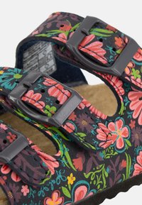 Sandales à motif floral avec un fond sombre, comprenant deux boucles réglables et une semelle texturée pour le confort.