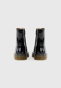 Bottines en cuir verni noir avec une finition lisse, fermetures éclair, bout rond et semelles en caoutchouc épaisses. Design simpliste avec un minimum de couture.