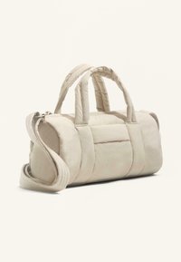 Jasnobeżowa pikowana torba z podwójnymi uchwytami do noszenia i odpinanym paskiem na ramię. Charakteryzuje się zaokrąglonym kształtem i fakturowaną tkaniną.