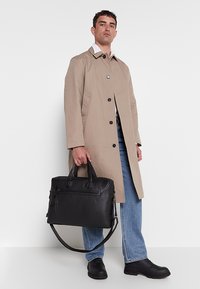 Black leather briefcase with dual handles and detachable shoulder strap. Features front zip pocket and structured design.