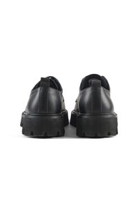 Scarpe in pelle nera con una suola spessa nera, dotate di punta arrotondata, design minimalista e linguetta sul retro.