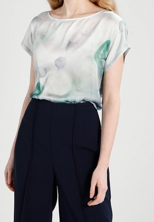 Blouse en soie dans des couleurs pastel douces avec un motif floral, présentant une coupe décontractée et des manches courtes. Associée à un pantalon taille haute bleu marine.