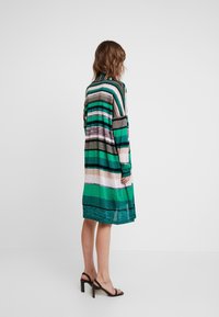 Raidallinen mekko, jossa on vihreitä, vaaleanpunaisia ja mustia sävyjä, pitkät hihat ja rento malli, joka ulottuu juuri polvien ylle. Sileä, kevyt kangas.