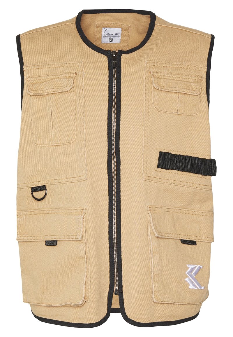 Khakifärgad väst med dragkedja framtill, svart kant, flera fickor fram och en dekorativ logotyp. Tillverkad av slitstarkt tyg med en mjuk struktur.