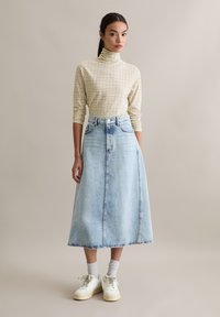 Licht geruit coltruitje in beige en geel; gecombineerd met een hoge taille, lange blauwe denim rok. Witte sneakers en boksokken.