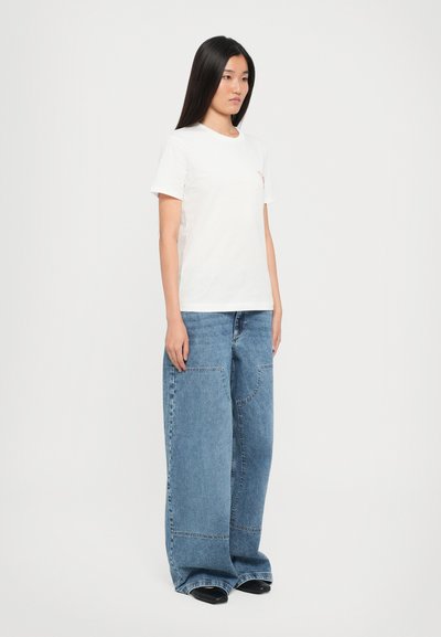 White cotton t-shirt with short sleeves, paired with oversized blue denim jeans featuring large pockets and a straight leg design. Black footwear.