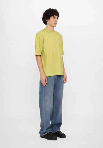 Light green short-sleeve t-shirt with a subtle circular pattern, paired with loose blue jeans and black shoes.