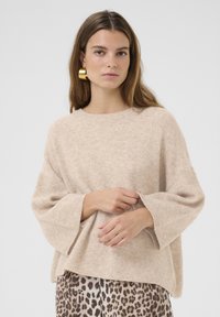 Beige, löst passande stickad tröja med breda ärmar och rund halsringning, bärs över en mönstrad leopardmönstrad kjol. Mjuk textur.
