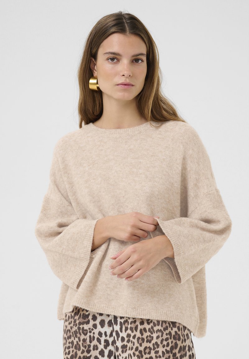 Beige, löst passande stickad tröja med breda ärmar och rund halsringning, bärs över en mönstrad leopardmönstrad kjol. Mjuk textur.