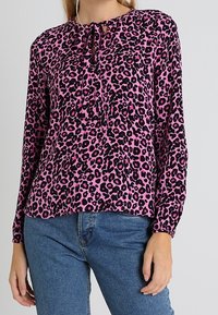 Rosa leopardmönstrad blus med långa ärmar, rund halsringning och en knytdetalj i mitten. Mjukt tyg och ledig passform. Kombinerad med blå jeans.