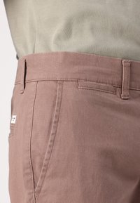 Pantalones de algodón rosa claro con corte recto, que cuentan con un bolsillo lateral, costuras cosidas y una pequeña etiqueta de la marca en la cinturilla.