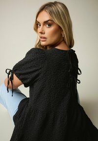 Top nero con tessuto texturizzato, maniche corte a sbuffo e lacci ai polsini e sul retro. Vestibilità ampia con orlo svasato.