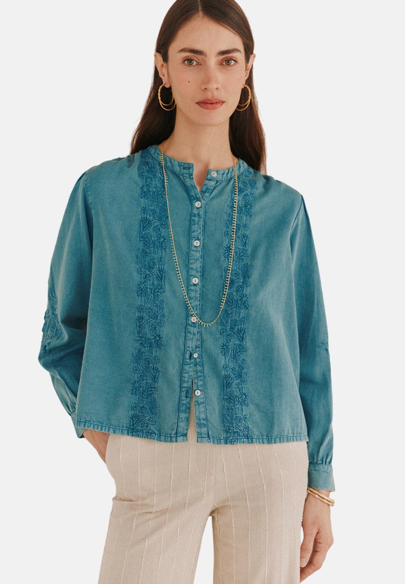 Hellblaues Denim-Hemd mit langen Ärmeln, Knopfleiste, filigraner floraler Stickerei entlang der Mitte und lockerer Passform.