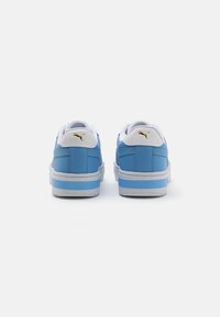 Sapatilhas de couro azul com detalhes brancos e logótipo dourado. Possuem uma superfície texturizada, colarinho almofadado e sola de borracha branca com faixa azul.