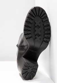 Stivale in pelle nera con suola in gomma testurizzata, dotata di un battistrada a motivo multiforme e cerniera laterale. Nome del marchio "Vagabond" visibile.