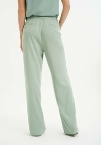 Jasnozielone spodnie typu wide-leg z miękkiego materiału, o prostym kroju, z bocznymi kieszeniami oraz tylnymi kieszeniami z delikatnymi detalami szwów.