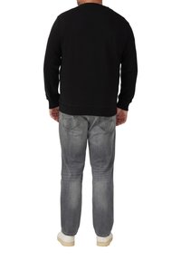 Felpa nera con colletto a girocollo e polsini a coste, abbinata a jeans grigi chiari. Le scarpe sono bianche con suola testurizzata.