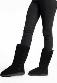 Black suede knee-high boots with a soft texture, rounded toe, and flat rubber sole. Folded cuff design at the top adds detail.