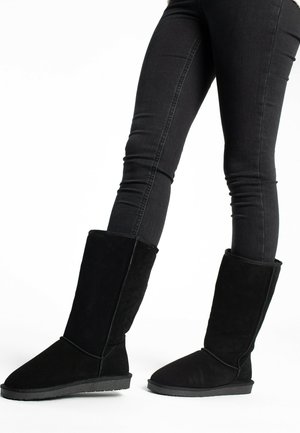 Black suede knee-high boots with a soft texture, rounded toe, and flat rubber sole. Folded cuff design at the top adds detail.