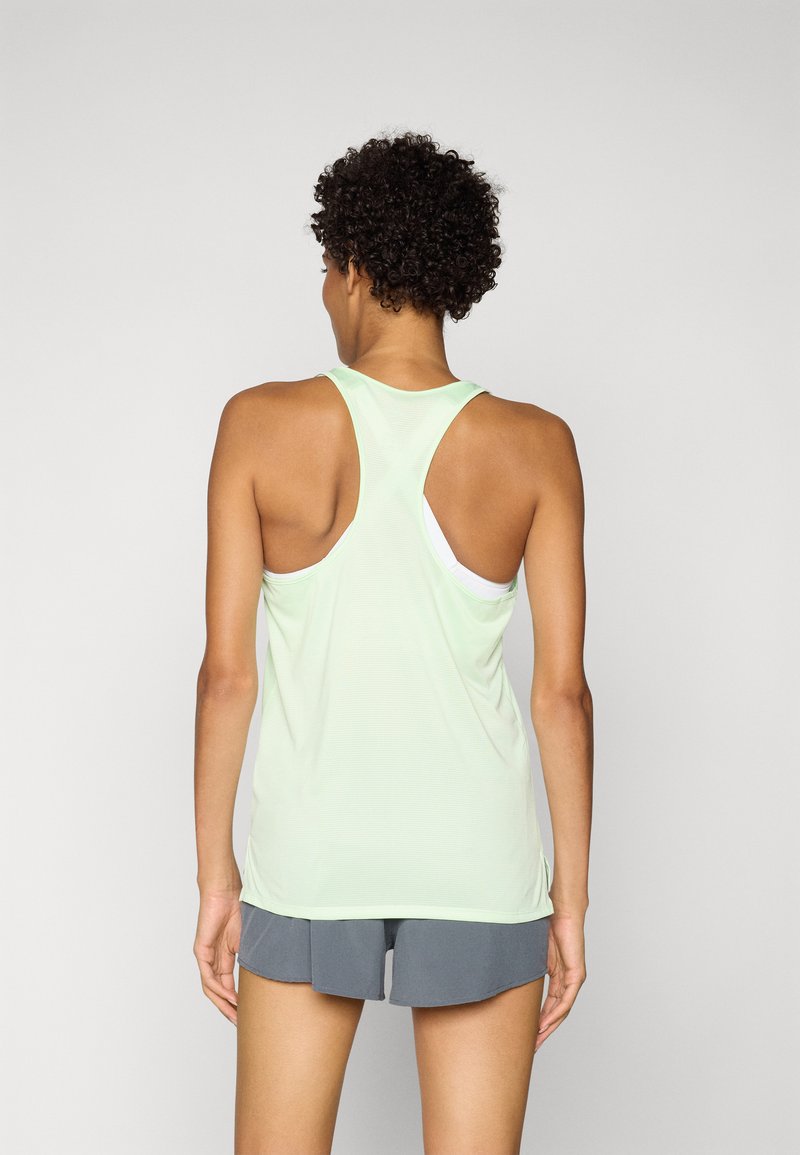 Débardeur sans manches vert clair avec un design dos nageur, fabriqué dans un tissu doux et respirant avec une texture côtelée subtile. Assorti avec des shorts gris.