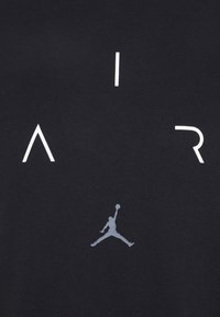 Černá látka s velkými bílými písmeny tvořícími slovo "AIR" a šedým logem Jumpman, s hladkou texturou a minimalistickým designem.