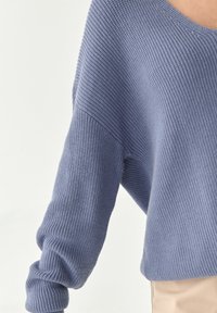 Manche de pull en tricot lavande doux et épais avec couture d'épaule tombante et poignets côtelés portée avec un pantalon beige clair.