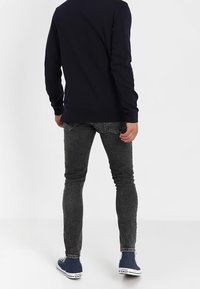 Camisa de manga larga de color marino combinada con jeans ajustados negros desgastados y zapatillas de lona marinas con suelas blancas. Diseño simple, con un mínimo de detalles.