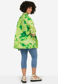 Giacca oversize verde tie-dye in tessuto texturizzato, con maniche a tre quarti e orlo curvo, abbinata a jeans blu cropped e sandali beige.
