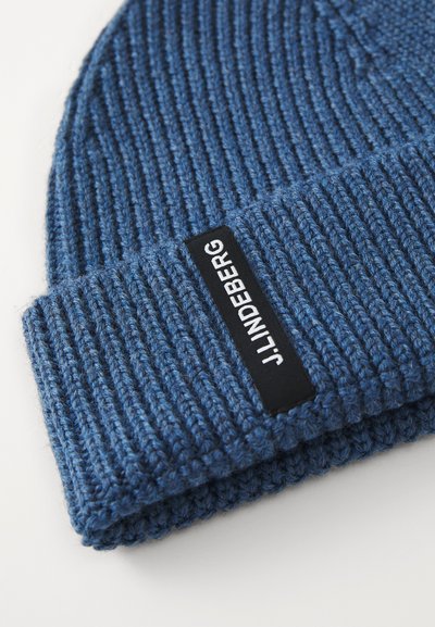 Blue knitted beanie with a ribbed texture and a folded cuff. Features a rectangular black label with white text.