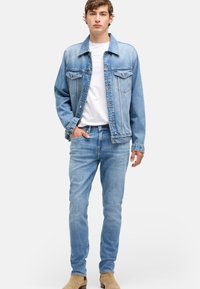 Lichtblauwe spijkerjas met twee borstzakken, gecombineerd met lichtblauwe spijkerbroek en een wit T-shirt. Soepele textuur, klassiek ontwerp.