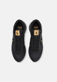 Svarta sportiga sneakers med en texturerad överdel, snörningsdesign, guldiga logotypdetaljer och en svart sula. Har en vadderad krage för komfort.