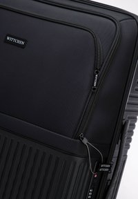 Valise rigide noire, avec texture striée, fermeture éclair et marque WITTCHEN. Équipée d'un cadenas à combinaison et de roues lisses.