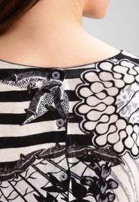 Baksidan av en person som bär en svartvit randig blus med blommönster och tre små svarta knappar längs den övre ryggen.