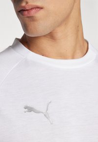 Biała bawełniana koszulka z okrągłym dekoltem i krótkimi rękawami raglanowymi, z haftowanym srebrnym logo Puma na obszarze klatki piersiowej.